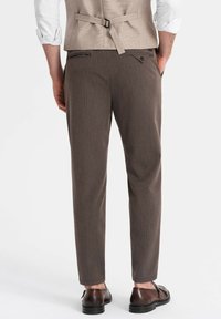 Pantalones a rayas marrones con un corte ajustado, que presentan una textura suave y bolsillos traseros, combinados con zapatos de vestir oscuros.