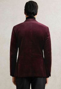 Blazer in velluto borgogna con colletto a punte, chiusura con un bottone e vestibilità su misura. Presenta una texture liscia e maniche lunghe con dettagli a bottone.