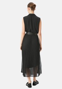 Schwarzes ärmelloses Kleid mit einem Kragenhalsauschnitt, transparenter plissierter Textur, gepunktetem Muster und einem taillierten Gürtel. Midi-Länge bis zur Wade.