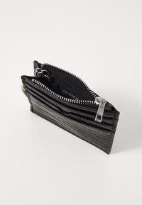 Cartera negra con relieve de cocodrilo, con múltiples ranuras para tarjetas, bolsillo con cremallera y detalles en metal plateado. Forma rectangular compacta.