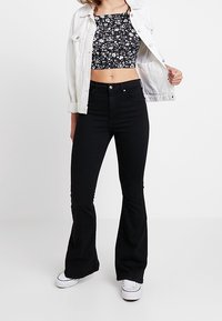 Černé rozšířené džíny s vysokým pasem, spárované s květinovým crop topem a bílou džínovou bundou, která má knoflíky a kapsy.