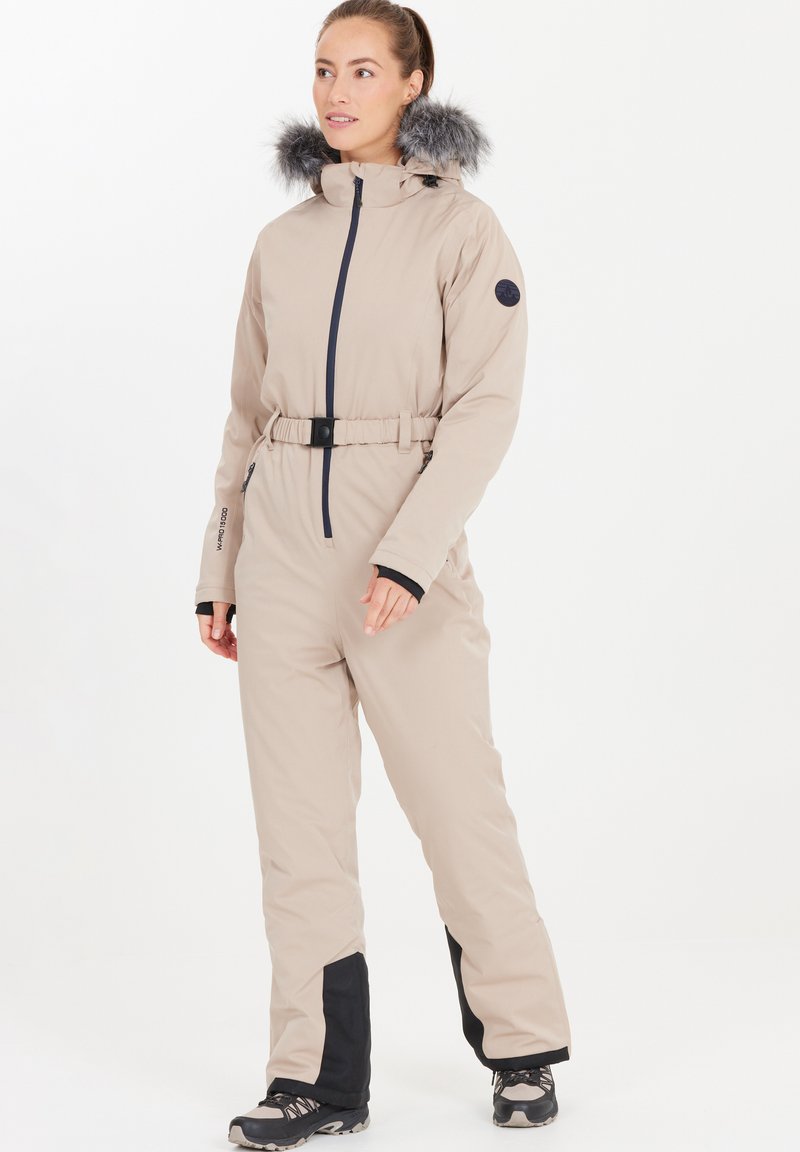 Beige vinteroverall med pälsfodrad huva, dragkedja fram, bälte i midjan, svarta detaljer vid ärmar och nedre ben, samt vattenavvisande tyg.