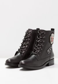 Mustat nauhattomat nilkkurit, jotka on valmistettu sileästä nahasta. Varustettu koristeellisilla paikoilla ja hopeisilla yksityiskohdilla. Satsimuotoista korkoa ja pyöreä kärki.