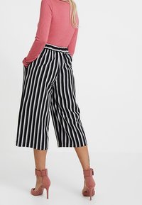 Černobílé pruhované culottes s širokými nohavicemi, elastickým pasem a bočními kapsami. Nosené s růžovými sandály na vyšším podpatku.