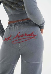 Grå sweatpants med broderad röd "ed hardy" text på baksidan, med avslappnad passform och elastisk midja. Slätt bomullstyg.