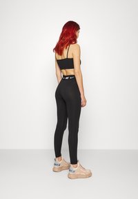 Top scurt sport negru și colanți cu talie înaltă. Modelul poartă teniși roz deschis cu un logo pe spate.