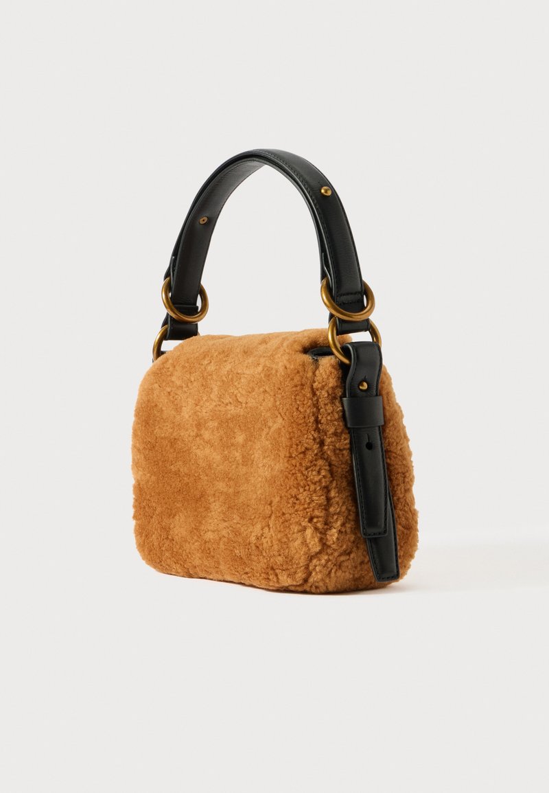 Piccolo handbag rettangolare in shearling marrone con tracolla in pelle nera e anelli dorati su sfondo bianco.