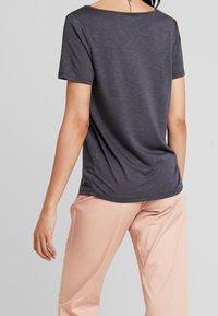 Mörkgrå t-shirt med avslappnad passform, korta ärmar och vid halsringning. Slät textur med diskret melerat mönster. Bärs tillsammans med ljusrosa byxor.