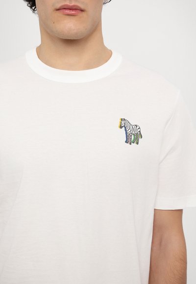 Balts kokvilnas T-krekls ar apaļu kaklu un īsām piedurknēm, uz kreisā krūtīs ir daudzkrāsains zebras grafiks.