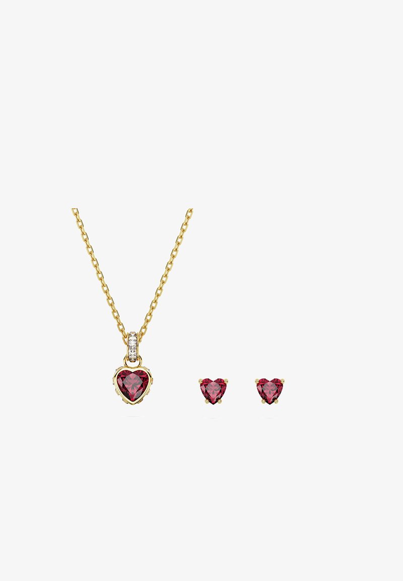 Colar de ouro e brincos combinando com pedras preciosas vermelhas em forma de coração, corrente do colar com pequenas pedras claras no laço do pendente.