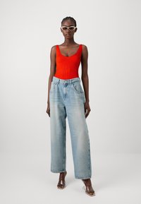 Rode geribde bodysuit met brede bandjes, gecombineerd met lichtblauwe baggy denim jeans met voorzakken. Heldere hakkenandalen zijn inbegrepen.