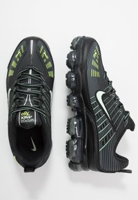 Czarne buty sportowe z teksturowaną cholewką, z zielonymi akcentami, widoczną jednostką amortyzującą powietrze oraz wyraźnym logo Nike.