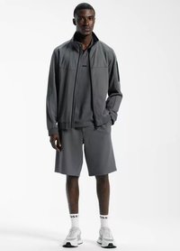 Grijze sportoutfit met een ritsjack, een T-shirt met korte mouwen en knielange shorts. Draag het met witte sneakers en merk sokken.