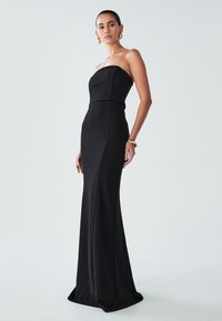 Melnas strapless kleitas ar pieguļošu augšu un plūstošu svārku. Izgatavota no gluda auduma, ar vertikālām šuvēm, nodrošinot elegantu siluetu.
