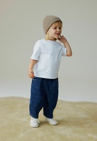 Camiseta blanca de manga corta, pantalones de mezclilla azul con lunares y zapatos blancos. El niño lleva un gorro beige acanalado. Textura suave en general.
