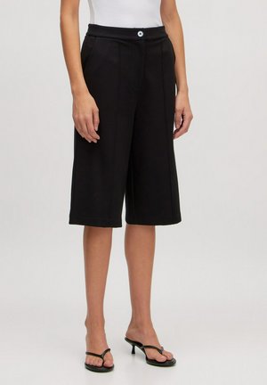 Schwarze Culottes mit mittelhoher Taille, vorderen Falten und einem einzigen Knopfverschluss. Die Materialien wirken glatt und bieten eine lässige, weite Silhouette.