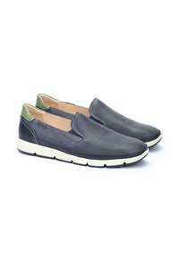 Zapatos de piel azul marino tipo slip-on con diseño perforado, acento en verde en el talón y suela de goma blanca. Construcción ligera y flexible.