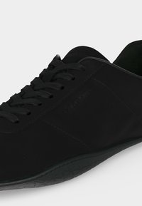 Baskets en cuir noir à profil bas avec lacets noirs et semelle texturée, marque Calvin Klein sur le côté.