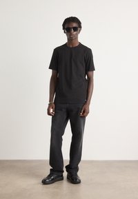 Tricou negru din bumbac, asociat cu blugi negri și teniși negri. Accesoriile includ ochelari de soare și un brățară din argint.