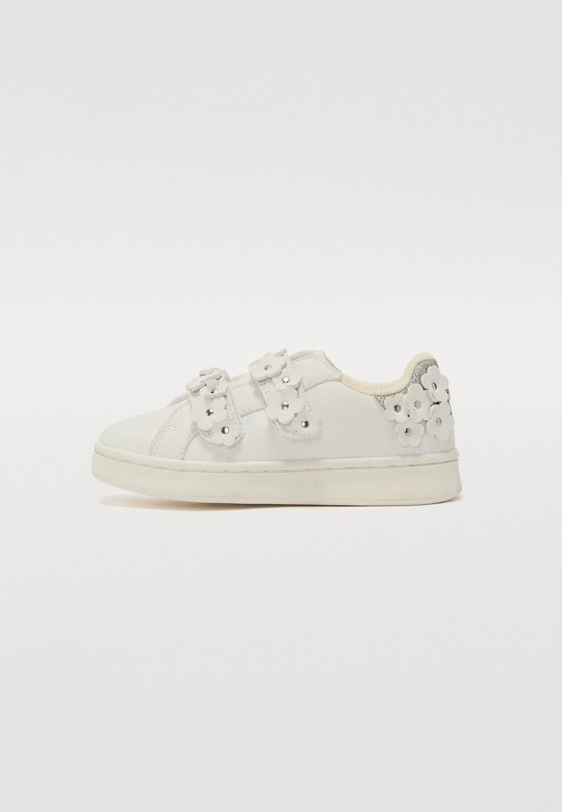 Zapatillas blancas con parte superior de cuero liso, aplicaciones florales y correas dobles. Suela de goma plana y diseño de punta redondeada.