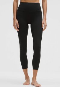 Leggings negros de cintura alta fabricados con un tejido elástico, con una textura suave y un diseño ajustado que termina en el tobillo.