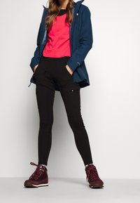 Granatowa wodoodporna kurtka, różowa koszulka z krótkim rękawem, czarne rozciągliwe spodnie typu cargo oraz ciemnoczerwone buty trekkingowe na sznurówki z fakturowaną cholewką.