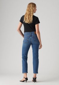 Vaqueros de mezclilla azul con corte recto, cintura alta y bolsillos traseros. Combinados con una camiseta negra de manga corta y zapatos de tacón negros.