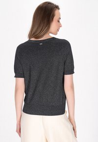 Kortærmet sort sweater med metallisk shimmer, rund hals og afslappet pasform. Har en ribbet kant og en subtil mærkebadge på bagsiden.