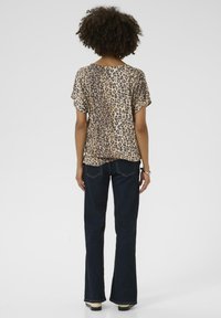 Skjorta med leopardmönster och kort ärm, rundad halsringning, bärs med mörka utsvängda jeans och stövlar, sedd bakifrån.