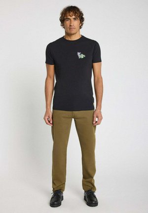 T-shirt noir à manches courtes avec un design floral brodé sur la poitrine gauche, associé à un pantalon olive et des chaussures noires.