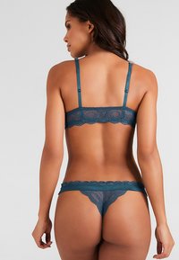 Teal kanten bh en string set met verstelbare bandjes, golvende randen en doorzichtige textuur. Achteraanzicht toont ingewikkelde kantdetails.