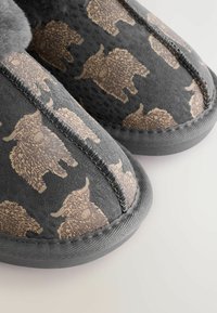 Gray slippers featuring a textured surface with a pattern of gold-colored, fuzzy animals. Stitching outlines the shoe edges.