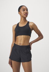 Crni sportski crop top s širokim trakama i glatkom teksturom, uparen s crnim hlačama visokog struka koje imaju elastičnu traku.