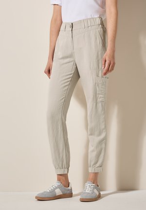 Lichtgrijze, taps toelopende broek met een elastische tailleband, zijzakken en ribgebreide boorden. G gedragen met grijs-witte sneakers.