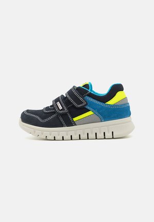 Baskets navy et teal avec des bandes velcro, en suède texturé et mesh, avec des détails d'accent jaune et une épaisse semelle en caoutchouc blanc avec des rainures.