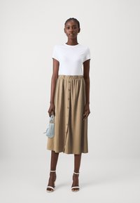 T-shirt bianco a maniche corte abbinato a una gonna khaki al ginocchio con chiusura a bottoni e vita elastica. Accessoriato con una borsa azzurro chiaro.