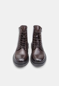 Botines de piel marrón con un diseño elegante, que presentan punteras redondas, cordones y una cremallera lateral. Superficie texturizada con un acabado suave.