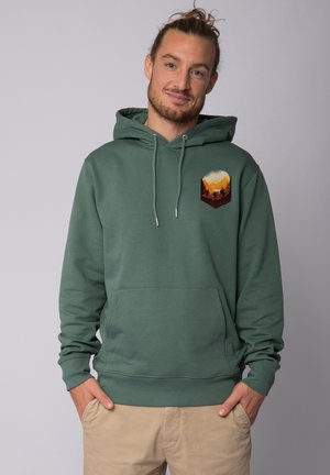 Groene katoenen hoodie met een voorkantzak, trekkoorden en een grafisch ontwerp van een berglandschap in warme kleuren op de linkerkant van de borst.
