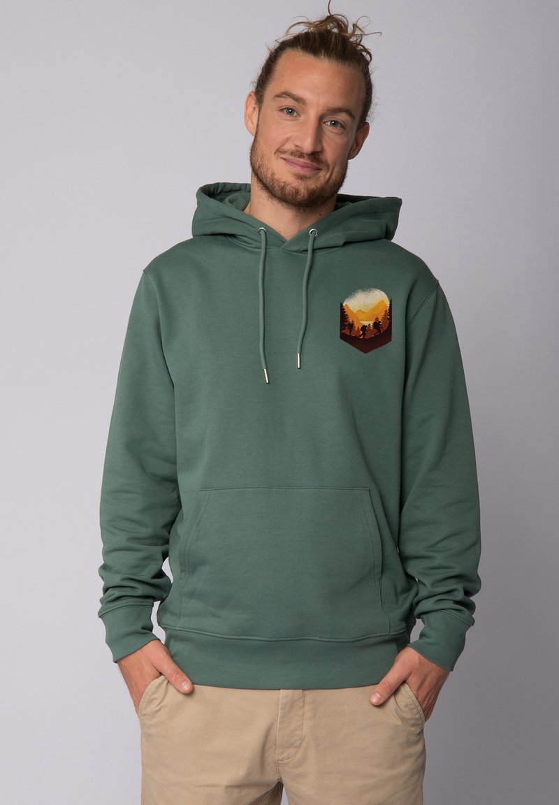 Hoodie en coton vert avec une poche frontale, des cordons de serrage et un graphique de scène de montagne dans des couleurs chaudes sur la partie gauche de la poitrine.