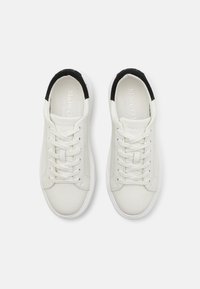 Bílé kožené tenisky s černými semišovými akcenty, kulatá špička, plochá bílá podešev a kontrastní tkaničky. Logo potištěné uvnitř.