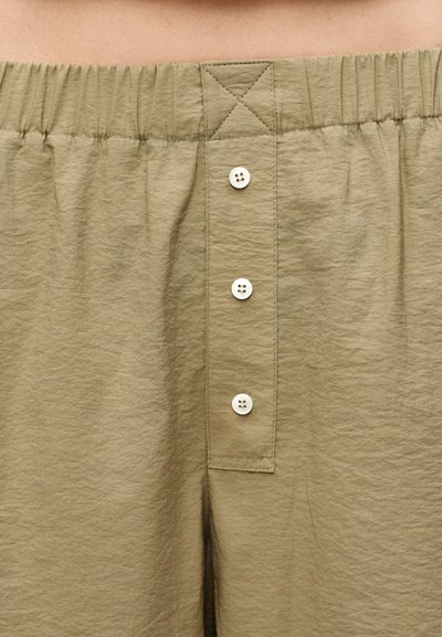 Σορτς ανοιχτού καφέ με ελαστική μέση, τρία λευκά κουμπιά μπροστά και ορατές ραφές.