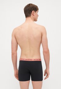 Fekete boxer nadrág rózsaszín derékrésszel, amelyen a "PIER ONE" felirat található. Az anyag simának és testhez simulónak tűnik, egyszerű dizájnnal.