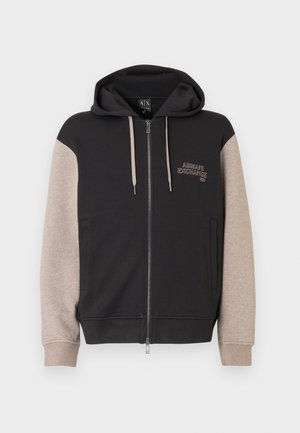 Sudadera con capucha y cremallera, con cuerpo negro y mangas beige. El material es suave con una textura lisa. Logo de la marca en el pecho en un color contrastante.