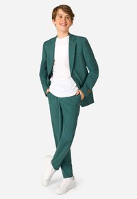 Blazer turchese e pantaloni abbinati con una texture liscia, abbinati a una t-shirt bianca e sneakers bianche. Il blazer presenta un sottile accento arancione.