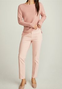 Suéter texturizado rosa claro de mangas largas, combinado con pantalones rosa claro de corte slim. Tacones rosa claro de punta cuadrada.