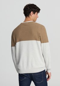 Sweter w kolorze kremowym i brązowym, podzielony na bloki kolorów, z prążkowaną teksturą w górnej części i gładkim materiałem w dolnej, z okrągłym dekoltem.