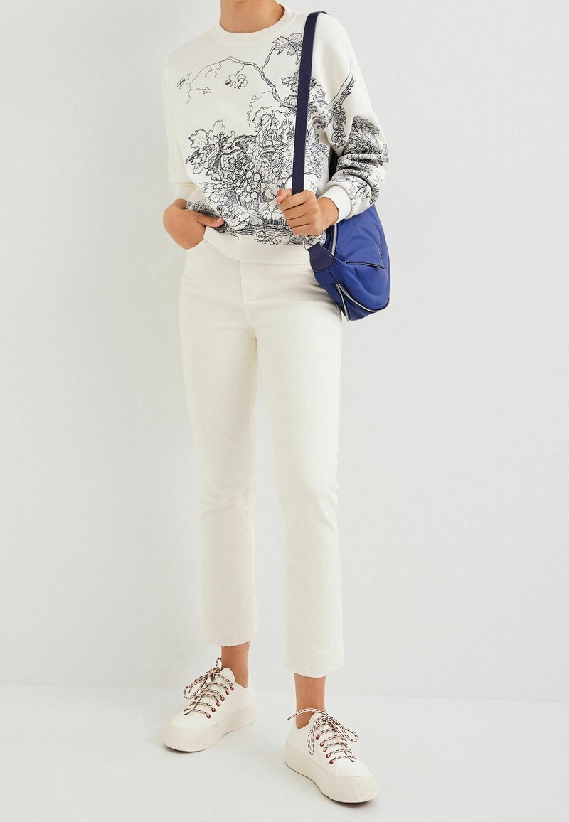 Valkoinen collegepaita, jossa on mustaa viivataidetta, valkoiset lyhyet housut ja valkoiset platsolettitossut monivärisillä nauhoilla, yhdistettynä siniseen laukkuun.