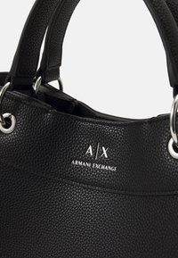 Czarna torebka skórzana o teksturowanej powierzchni z podwójnymi uchwytami i srebrnym logo Armani Exchange w pobliżu górnej krawędzi.