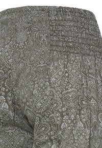 Tissu vert olive avec un motif paisley et floral blanc complexe, montrant un détail de ceinture élastique froncée.