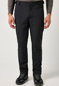 Pantalones exteriores negros con una textura suave y ligera, con cierre de cremallera y botón, usados con zapatos de senderismo negros.